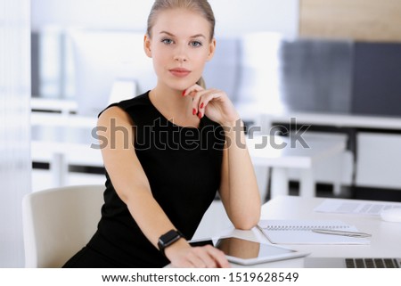 Business woman working with tablet computer while sitting at the desk in modern office. Secretary or female lawyer looks beautiful in black dress. Business people concept
