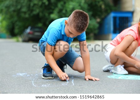 Little child drawing with chalk on asphalt. Outdoor play