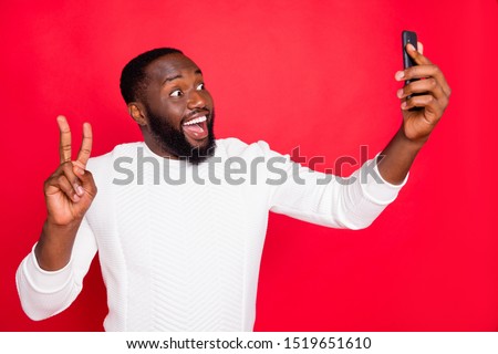 Hello dear followers! Photo of funny dark skin man holding telephone making selfies showing v-sign symbol wear white knitted sweater isolated red background