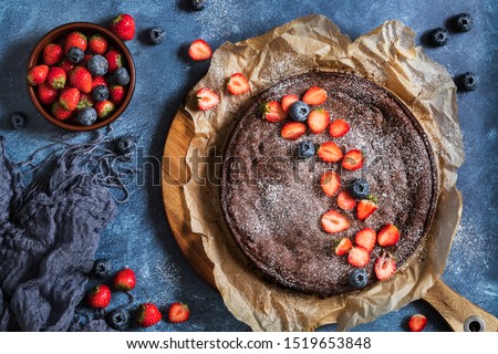 Swedish traditional chocolate cake Kladdkaka with fresh berries, strawberries and blueberries. On a blue background, seen from above flat lay perspective.