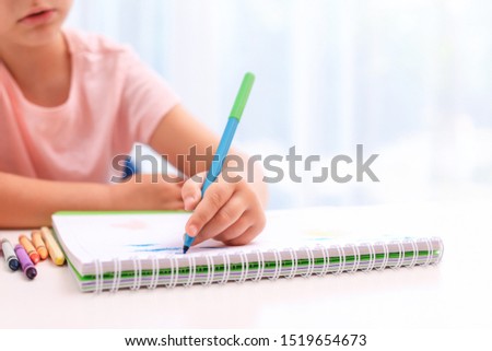 Little left-handed girl drawing at table in room, closeup