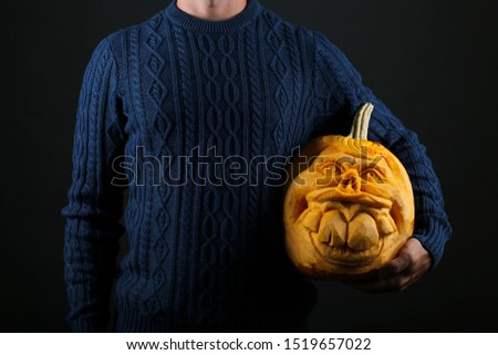 Studio shot of young man wearing blue knitted sweater with jack o lantern. Portrait of hipster male holding halloween pumpking by his side. Background, close up, copy space, isolated.