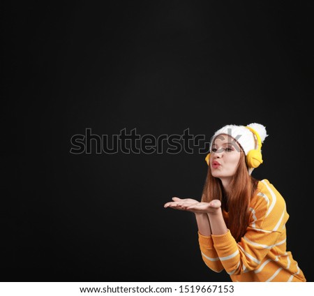 Young woman listening to music with headphones on black background, space for text