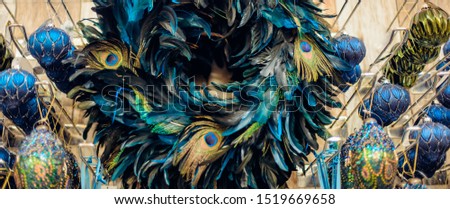 Close up peacock feather wreath with navy blue and golden balls in shop's display. Close up creative modern Christmas tree decor. Exotic New Year. Trendy colours. Wide banner