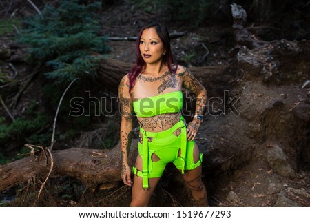 Asian tattooed woman in neon rave clothing poses in a redwood forest at night