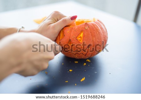 A woman carves face on a pumpkin for a Halloween lamp on a black table. Close-up female hands making Jack-o'-lantern to the eve of all saints..