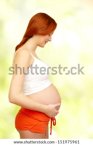 beautiful pregnant woman tenderly looking at her belly over green background
