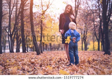 Little blond boy hid behind a yellow leaf. Wants to give mom. Autumn park on the background