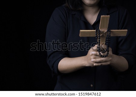 A woman hand holding a wooden cross on an isolated black background