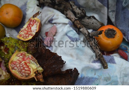 Open pomegranates, brown leaves and persimmons, placed on fabrics and floors