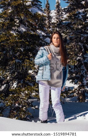 Portrait of a young beautiful brunette woman with blue eyes and freckles on face in winter snowy mountain landscape. Beautiful girl in the winter outdoors dreesed in sweater and blue jacket.