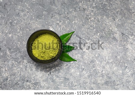 Matcha green tea powder in a black ceramic bowl on concrete surface. It is a rich source of antioxidants and polyphenols. Selective focus with copy space in minimal style. Horizontal orientation.