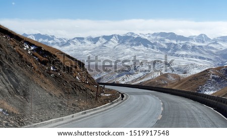 Scenic winter view from the asphalt road in the mountains covered with snow on a background of blue sky and clouds, road to snow mountain.