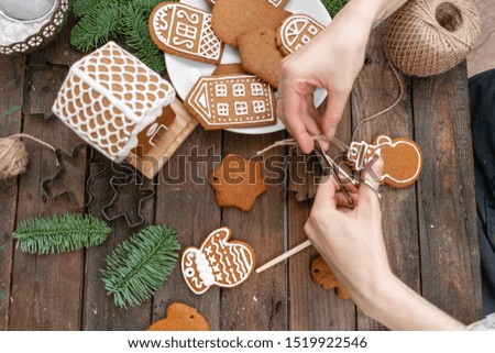 Icing of Christmas bakery. Woman decorating honey gingerbread cookies on wooden brown table. closeup, copy space. Blank biscuit gingerbread house, ready to decorate.