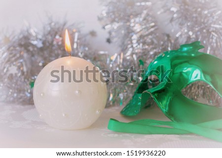 Green carnival mask and a burning candle close-up on a background of shiny tinsel. Christmas background