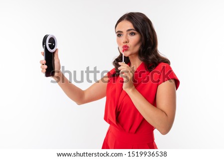 secretary on the background of a white wall corrects makeup, a girl looks in a smartphone and paints her lips