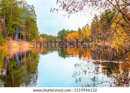 autumn landscape, in which the blue sky is reflected in the water of the river, a mixed forest with yellowed leaves on the trees grows along the banks
