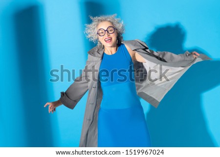 Cheerful lady. Cheerful fashionable curly woman wearing blue dress and grey trench coat