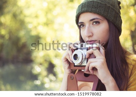 female photographer with fashionable  vintage camera outdoors taking photos of nature in autumn. creative artistic woman enjoying  photography with blur background bokeh of fall color leaves.