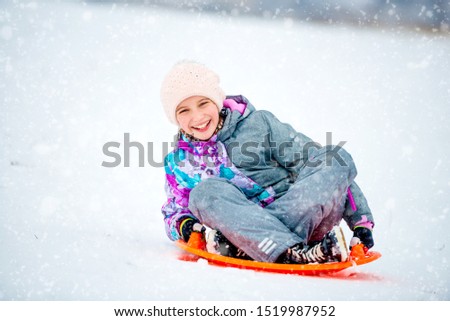 Happy little girl sliding down the hill on saucer sled. Girl enyoing slider ride on the snow