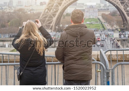 Tourists couple are taking photo and enjoying architecture in Paris in winter. Woman and man are traveling and sightseeing city attrcations on weekend vacation.