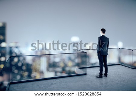 Businessman looking into the distance on rooftop with blurry night city view. Copy space. Success, vision and future concept 