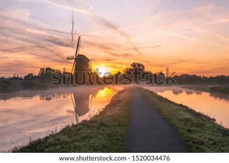 Typical dutch landscape image with windmill and fog over the water at sunrise
