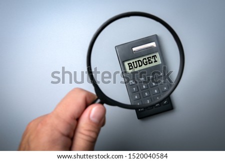 Budget concept. Calculator on white table. Man's hand, holding magnifying glass