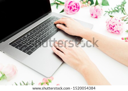 Woman typing on laptop. Workspace with female hands, laptop and pink flowers on white.