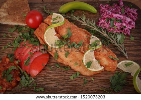 Fried fish fillet, with vegetables and salads, wooden background
