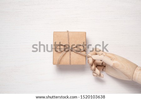 Wooden mannequin hand opens a gift in a box tied with twine. Gift background concept for holiday makers. Greeting card for christmas, birthday and new year.