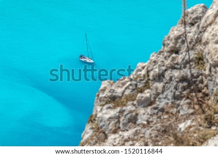 A yacht docked in a bay with rocky mountains around and turquoise water on a sunny day