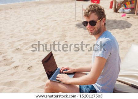 Young business man working on laptop on the beach in sunny day, freelance job online. Vacation, lifestyle and work concept.