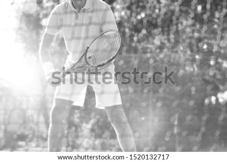 Black and white photo of senior athlete standing in court and playing tennis