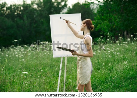beautiful woman outdoors paints an easel picture