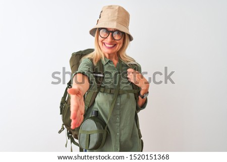 Middle age hiker woman wearing backpack hat canteen glasses over isolated white background smiling friendly offering handshake as greeting and welcoming. Successful business. Royalty-Free Stock Photo #1520151368
