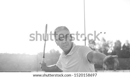 Black and white photo of senior athlete hitting ball with tennis racket in court