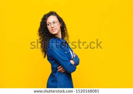 young pretty woman smiling gleefully, feeling happy, satisfied and relaxed, with crossed arms and looking to the side against orange wall