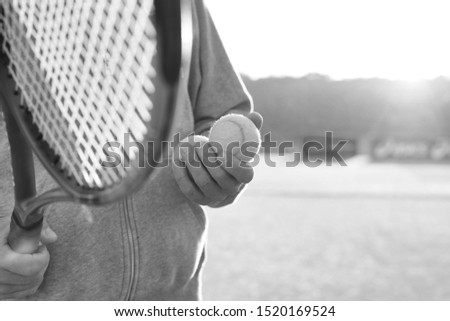 Black and white photo of Man holding tenis racket and ball at court on sunny day