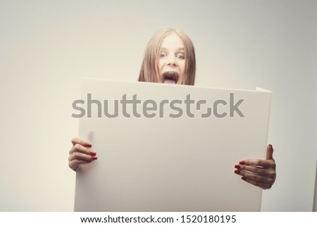 Fashion pretty girl holding white board with place for text. Shocked girl looking on camera