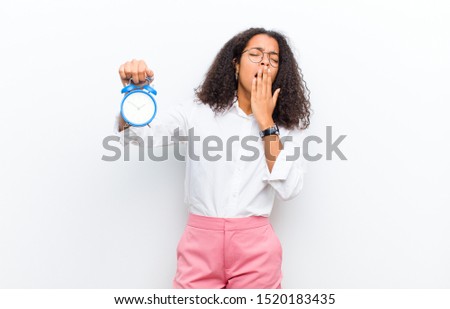 young pretty black woman with an alarm clock against white wall