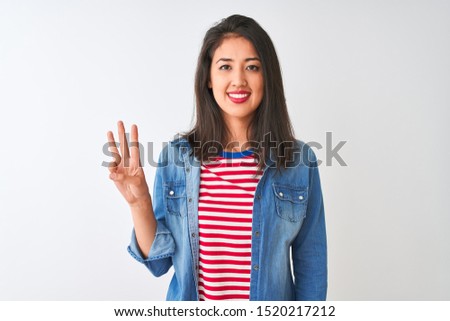 Young chinese woman wearing striped t-shirt and denim shirt over isolated white background showing and pointing up with fingers number three while smiling confident and happy.
