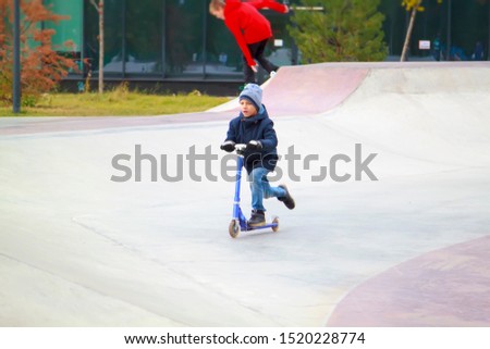 boy on kick scooter trains to ride and perform tricks like older guys in skate park