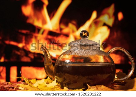 glass teapot on a table with autumn leaves on a background of a burning fireplace