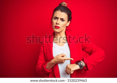 Young beautiful business woman standing over red isolated background In hurry pointing to watch time, impatience, upset and angry for deadline delay