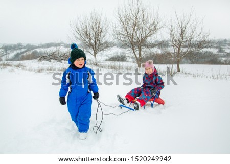 Happy boy and girl sledding from a hill in winter. Winter games outdoors. Winter vacation.