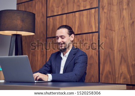Image of happy businessman sitting at table with laptop on background of wooden wall.