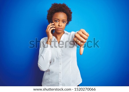 African american woman talking on the smartphone over blue isolated background with angry face, negative sign showing dislike with thumbs down, rejection concept