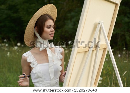 young woman draws a picture in a white summer dress on nature