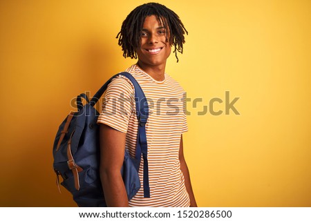 Afro american student man with dreadlocks wearing backpack over isolated yellow background with a happy face standing and smiling with a confident smile showing teeth